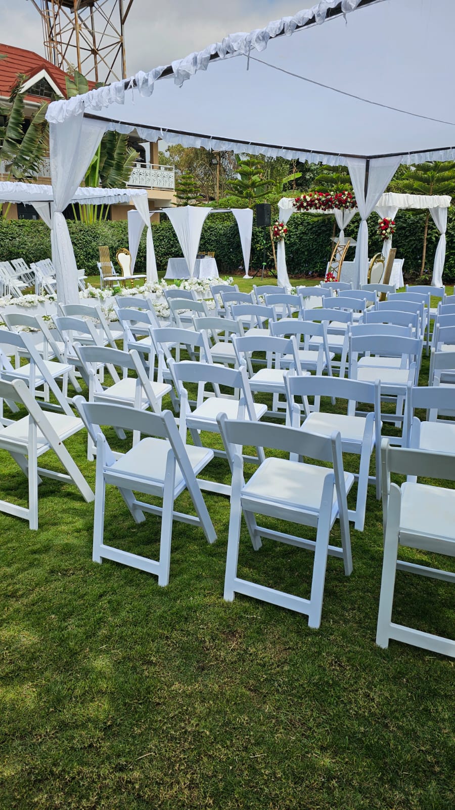 White folding chairs set in rows under a draped canopy facing a floral wedding altar on the garden lawn