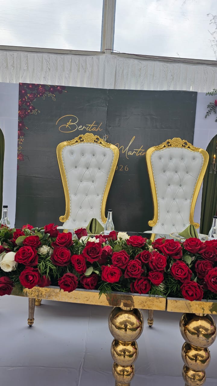 Gold head table topped with red roses and two ornate white and gold chairs against a backdrop