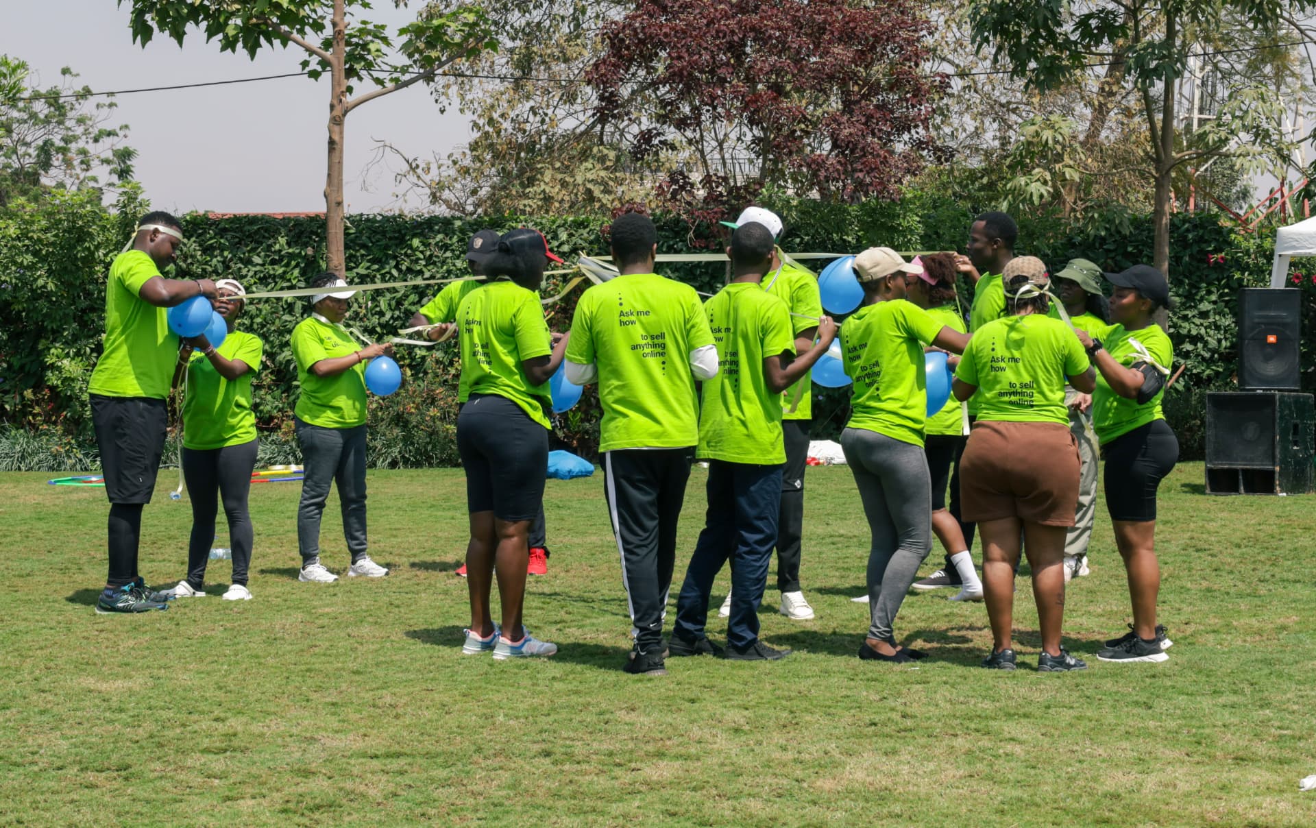 Team in bright green shirts working together with blue balloons on the garden lawn