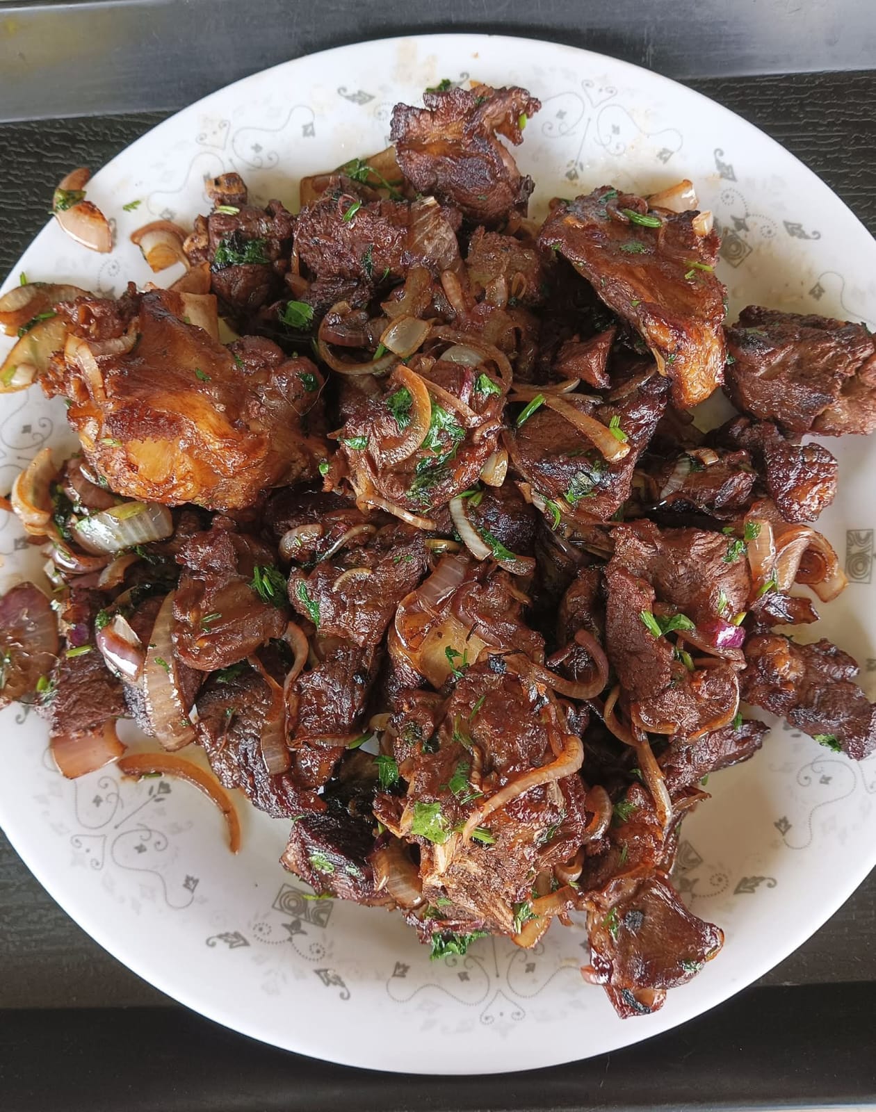 A platter of nyama choma with onions and fresh herbs