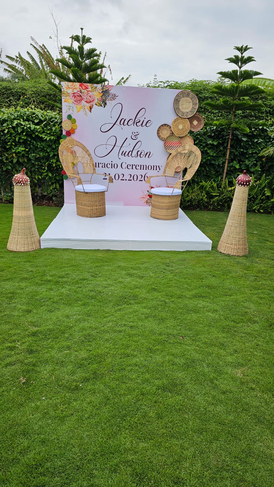 Traditional ceremony stage with woven Kenyan baskets, cane chairs and a personalised backdrop on the lawn